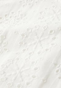 Vitt tyg med intrikat broderi med blommönster, cirkulära utskärningar och texturerade detaljer för ett ömtåligt utseende.