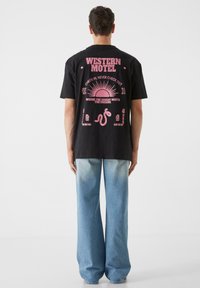 Must musta t-särk mustast puuvillast roosa graafilise trükiga, millel on tekst "Western Motel", päike ja dekoratiivsed elemendid. Kombineeritud helesiniste laiade teksadega.