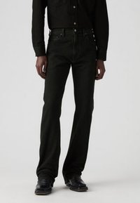 Donkergroene jeans met een rechte snit, vijf zakken, knoop- en ritssluiting, gemaakt van katoenstof, gedragen met een bijpassend zwart shirt.