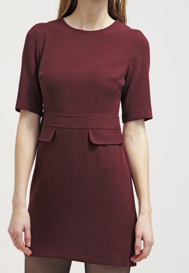 Vestido corto burdeos de manga corta con escote redondo, detalle de costura en el frente y dos bolsillos frontales en la cintura. Textura de tela suave.