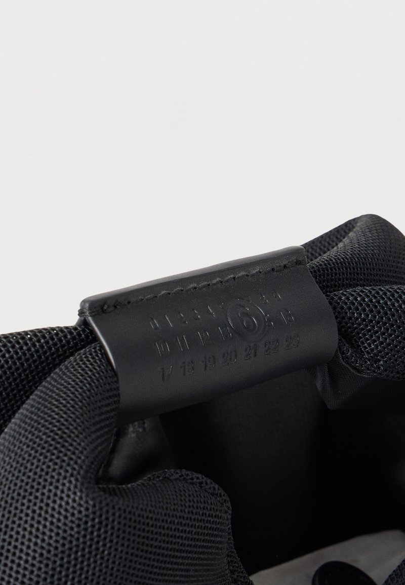 Black shoe interior with a leather size tag showing numbers 0 to 23, with size 6 circled, attached to padded mesh fabric lining.