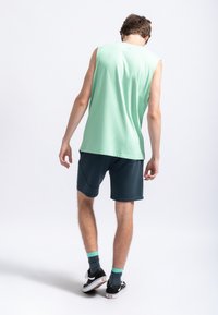 Maglietta senza maniche verde menta, pantaloni corti scuri, scarpe nere con accenti bianchi, calzini turchesi; tessuto morbido, vestibilità casual, design semplice.