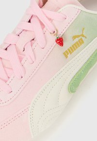 Roze suède Puma sneakers met lichtgroene en witte accenten en een klein rood aardbeiencharme aan de veters.
