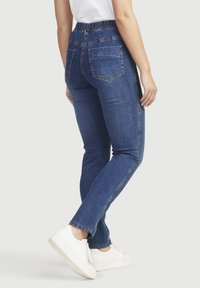 Siniset farkut, joissa on joustava vyötärö, suora lahje, takataskut ja vaaleat ompeluyksityiskohdat, yhdistettynä valkoisiin lenkkitossuihin.