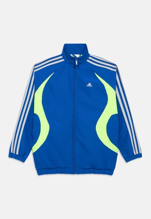 Giacca da corsa Adidas blu con pannelli laterali giallo neon curvi, maniche bianche a tre strisce, cerniera frontale e piccolo logo sul petto.