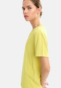 Żółta koszulka z dekoltem w serek i krótkimi rękawami, wykonana z miękkiego materiału. Projekt jest prosty, z prostym krojem i bez widocznych wzorów.