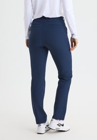 Marinblå träningbyxor med två bakfickor och en slät yta, tillsammans med vita träningsskor med en svart Nike-logotyp.