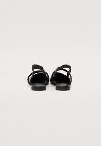 Sandales noires avec une sangle arrondie et texturée et une semelle plate. Présente un design nervuré le long de la sangle et un intérieur lisse.