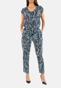 Jumpsuit blu navy con un motivo a zebre bianco vorticoso, caratterizzato da maniche corte, scollatura a V, vita elasticizzata e tasche frontali.