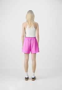 Shorts en coton rose avec une taille élastique et des poches latérales, associés à un débardeur blanc à côtes et des baskets noires.