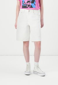 Hvite denimshorts med løs passform, høy midje, oppbrettede kanter og frontlommer, kombinert med hvite høye sneakers.