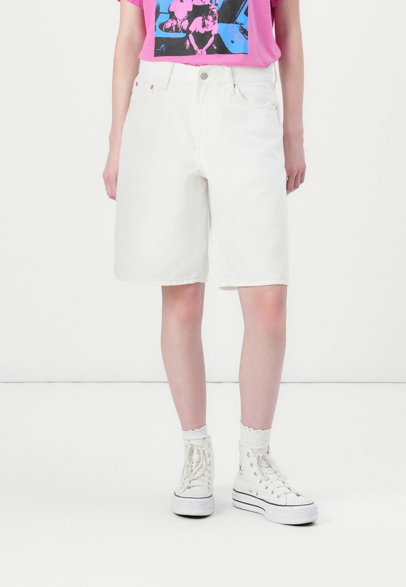 Hvite denimshorts med løs passform, høy midje, oppbrettede kanter og frontlommer, kombinert med hvite høye sneakers.