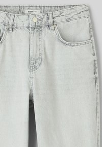 Jean en denim gris clair avec une finition délavée, dotée d'une taille haute, de cinq poches et d'une fermeture à bouton en métal. Texture usée au niveau des coutures.