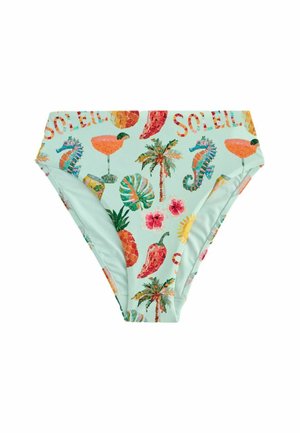 Kobieta uśmiechająca się w kolorowym bikini z tropikalnymi wzorami, stojąca obok drewnianej skrzyni wypełnionej grejpfrutami na zewnątrz w świetle słonecznym.