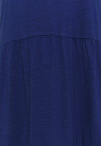 Głęboki niebieski materiał z zebranym szwem, tworzącym miękkie, pionowe fałdy oraz subtelny wzór tkany.