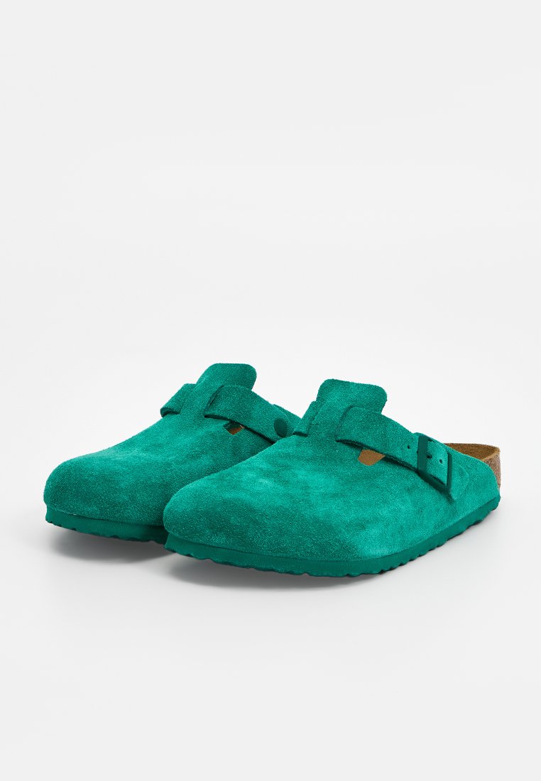 Zielone zamszowe klapki z płaską podeszwą, okrągłym noskiem i podwójnym zapięciem na klamrę. Miękka tekstura i prosta sylwetka.
