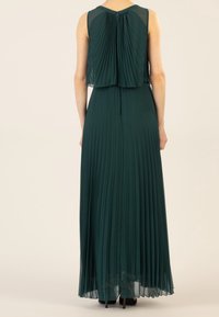 Robe longue plissée en vert foncé avec un corsage à plusieurs niveaux et un superposé transparent. Possède un dos en clef et une texture lisse et fluide.