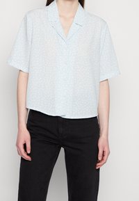 Short-sleeve, light blue blouse with a floral pattern, button front, and a relaxed fit. Made of soft fabric with a collar and a cropped design.