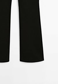 Jambes de pantalon noires à coupe évasée, photographiées sur fond blanc.