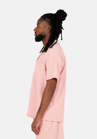 Kortärmad pikétröja i bomullsmix, rosa, med bröstficka och subtil textur. Modellen bär den tillsammans med matchande shorts, visad i profil.