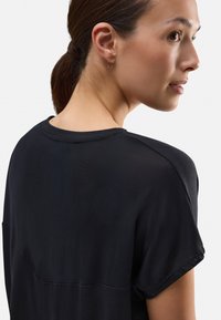 Camiseta negra de corte relajado, con mangas cortas enrolladas, tejido texturizado y un panel liso en contraste en la parte superior de la espalda.