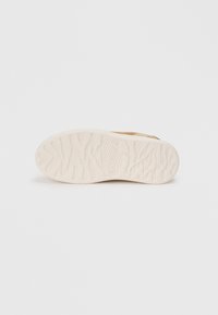 Semelle de chaussure en caoutchouc avec une finition blanche texturée. Présente un motif en vagues et une marque en relief. Le design est plat et fonctionnel.