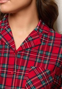 Camisa de pijama de algodón de cuadros rojos con un cuello con muesca, cierre de botones y un bolsillo en el pecho, con patrones de cuadros verdes y blancos en toda la prenda.