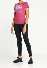 Fuchsia träningsskjorta med "RUN"-textmönster, parat med svarta tights och svarta skor, med texturerad tyg och strömlinjeformad design.