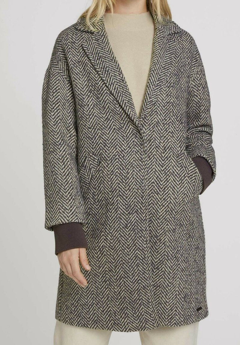 Cappotto in misto lana a motivo pied de poule con colletto a punta, tasche laterali e accenti scuri a contrasto sulle maniche, in tonalità di grigio e beige.