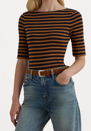 Donna che indossa una maglietta aderente a righe orizzontali blu navy e marroni con maniche al gomito, jeans blu a vita alta e cintura di pelle marrone.