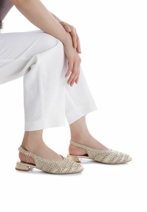 Zapatos slingback dorados con textura tejida, punta puntiaguda y tacón ancho. Correa adornada con detalles decorativos.