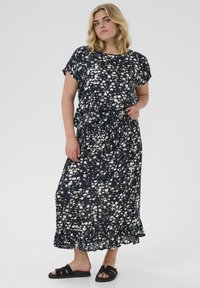 Abito maxi fluido navy a fiori con motivi di fiori bianchi sparsi, maniche corte e orlo volante. Abbinato a sandali neri flat.