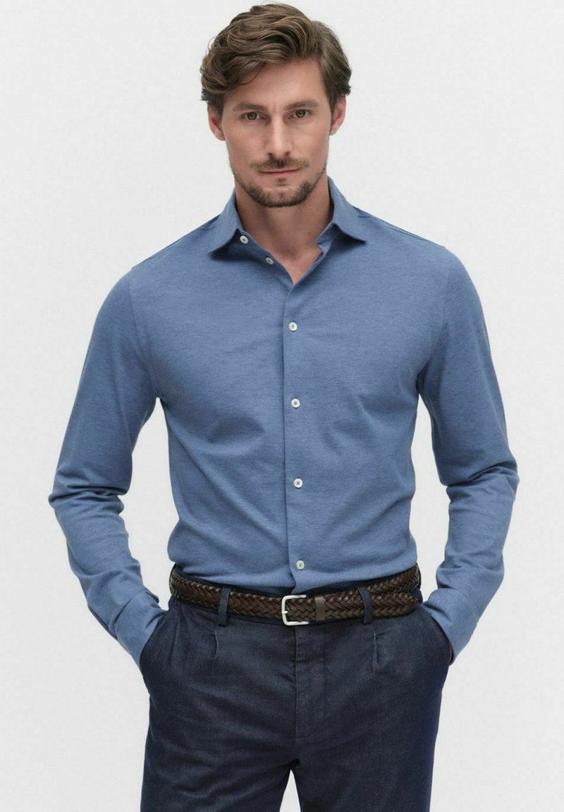 Blauw langamige shirt van zachte stof, voorzien van een klassieke kraag, knopen aan de voorkant en subtiele textuur, gecombineerd met donkere broek en een gevlochten riem.
