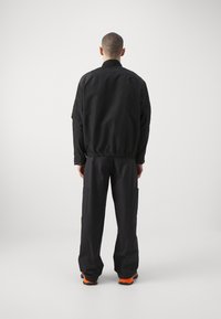 Mustmust musta bomber-jakk with elastsete ääred ja varrukad, millega on kokku sobitatud laiad mustad cargo-püksid küljetaskutega ja oranžide aktsentidega kingad.