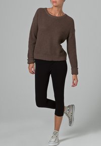 Bruine geribde trui met een wijde halslijn, gecombineerd met zwarte capri leggings en grijze sneakers. De outfit heeft een ontspannen pasvorm en een gestructureerde stof.