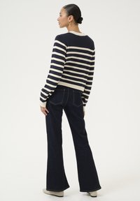 Striped knit sweater in navy and cream, fitted at the waist. Paired with dark flared jeans. Model facing away, showcasing the outfit's back.