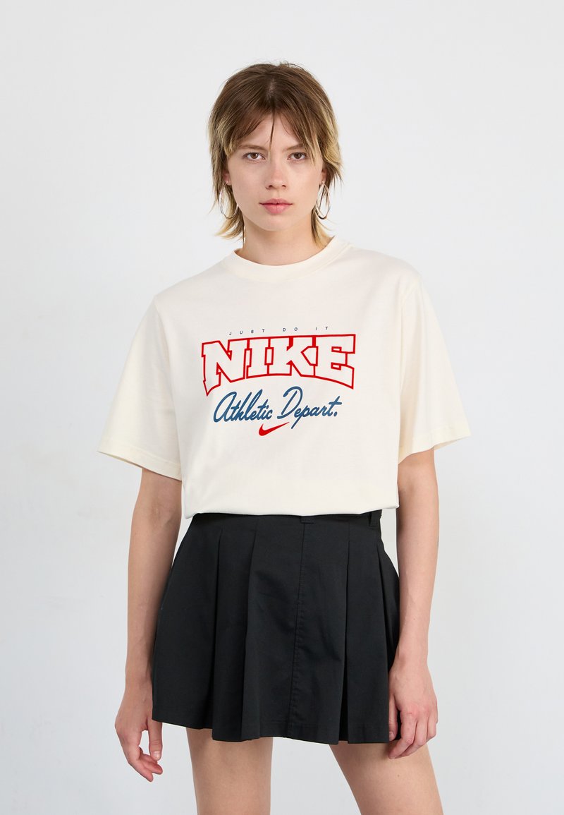 Crème-kleurige katoenen T-shirt met korte mouwen en een ronde halslijn, met een gedurfde rode en blauwe Nike-afbeelding op de voorkant.