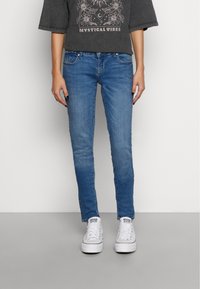 Jeans de denim azul claro com um corte slim, apresentando cinco bolsos e um desbotado subtil. Combinados com ténis brancos e uma t-shirt gráfica de mangas curtas.