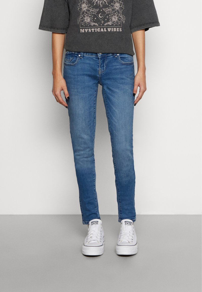 Jeans de denim azul claro com um corte slim, apresentando cinco bolsos e um desbotado subtil. Combinados com ténis brancos e uma t-shirt gráfica de mangas curtas.