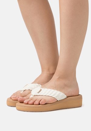 Hvide tov-sandaler med en tyk tan farvet platform. Overdelen har et flettet design med et bladmotiv. Åben tå-stil viser naturlige negle.