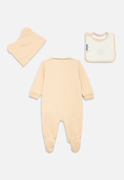 Beige baby footed romper, matching hat with bear ears, and beige-trimmed white bib with Moschino label on a white background.