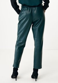 Green faux leather pants with a fitted waist, tapered legs, and a smooth texture. Worn with black high-heeled ankle boots.