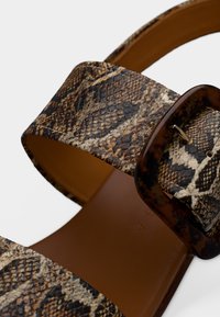 Καφέ και μαύρα σανδάλια με σχέδιο φίδι, με φαρδιά λουράκι, υφή στην επιφάνεια και ορθογώνια αγκράφα από υλικό που μοιάζει με χελώνα.