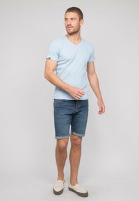 T-shirt V à manches courtes bleu clair associé à un short en denim noir aux manches retroussées et des chaussures beige à enfiler. Style décontracté avec un design simple.