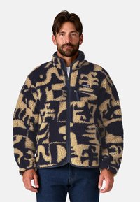 Giacca in fleece con zip frontale, caratterizzata da un motivo astratto blu navy e beige. Ha un colletto alto e una tasca sul petto con zip.