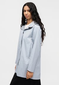 Svetlomodrá nepremokavá bunda s kapucňou, vybavená predným zipsom, čiernymi doplnkami na golieri a voľným strihom. Hladká textúra.