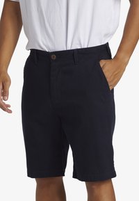 Pantalones cortos de algodón azul marino con cierre de botón, bolsillos frontales y dobladillo enrollado. La tela parece suave y resistente, ideal para uso casual.