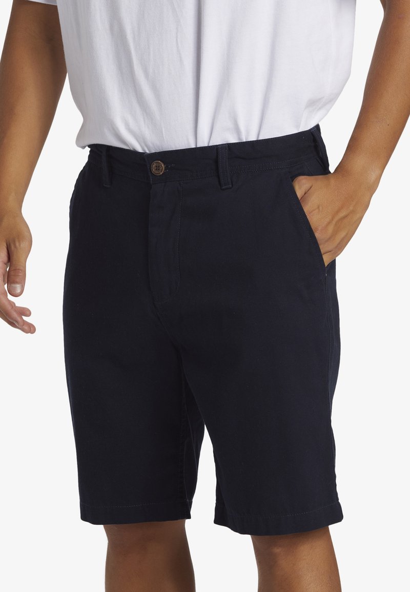 Pantalones cortos de algodón azul marino con cierre de botón, bolsillos frontales y dobladillo enrollado. La tela parece suave y resistente, ideal para uso casual.