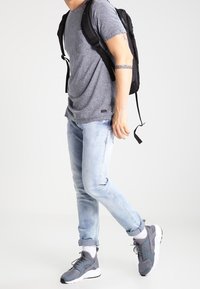 Šedé tričko s krátkým rukávem, světle modré džíny s otřepy, šedé tenisky s bílými podrážkami a černý batoh. Jednoduchý a ležérní outfit.