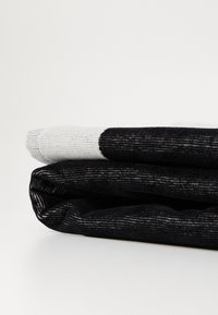 Zwart en grijs paar opgevouwen sokken met een gestreept textuur. De bovenkant heeft een lichtgrijze sectie met een stippenpatroon en een geribde boord.